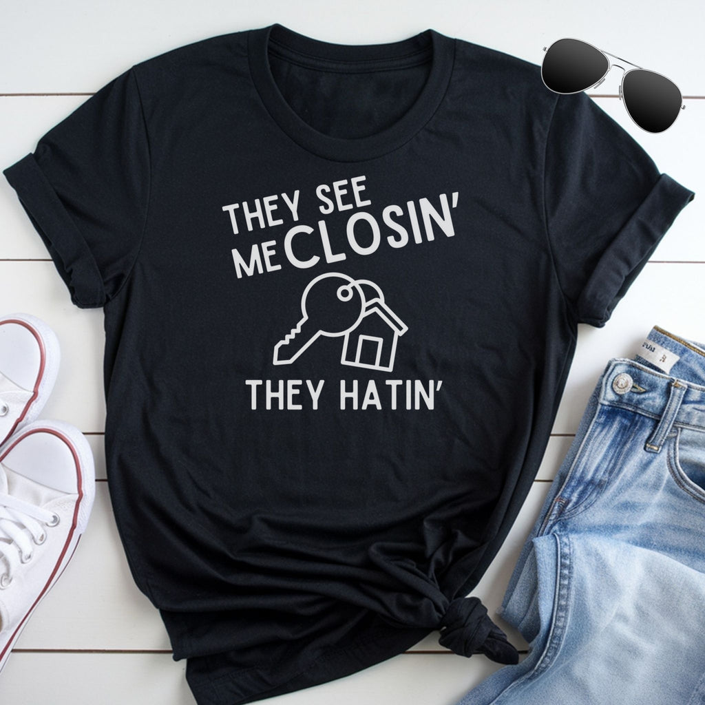 A black t-shirt with white text and a graphic design, along with a pair of jeans and sunglasses, all laid out on a white surface.