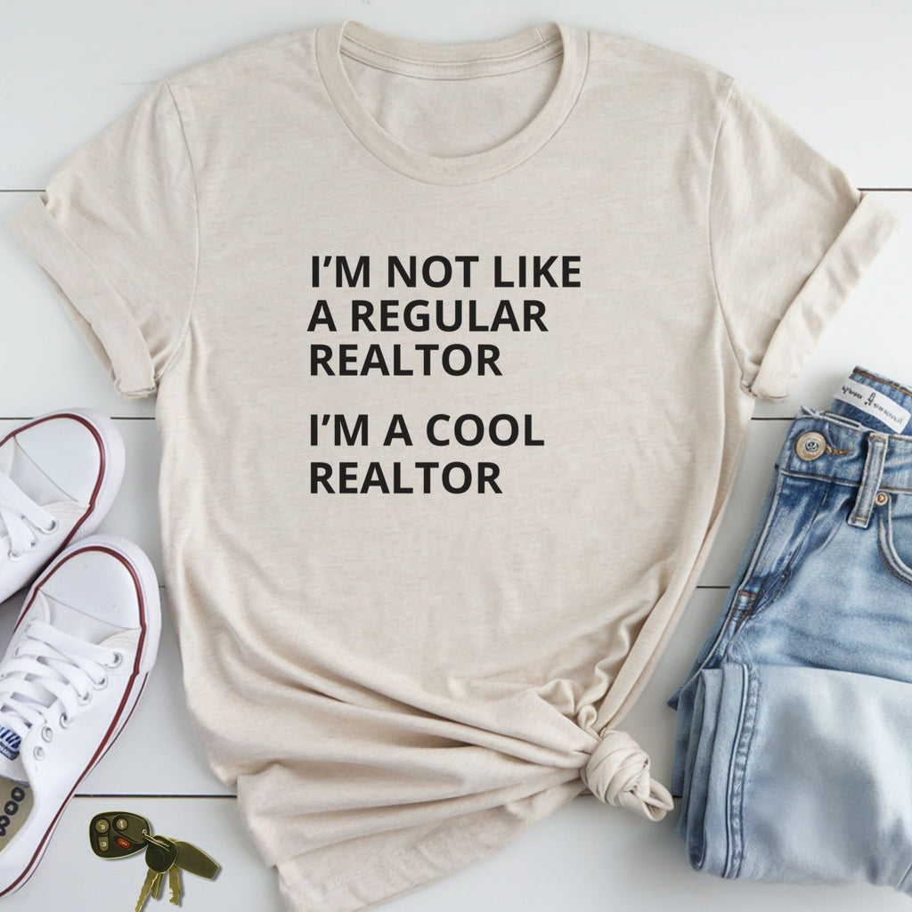 A beige t-shirt with the text "I'M NOT LIKE A REGULAR REALTOR I'M A COOL REALTOR" printed on it, along with a pair of jeans and sneakers.