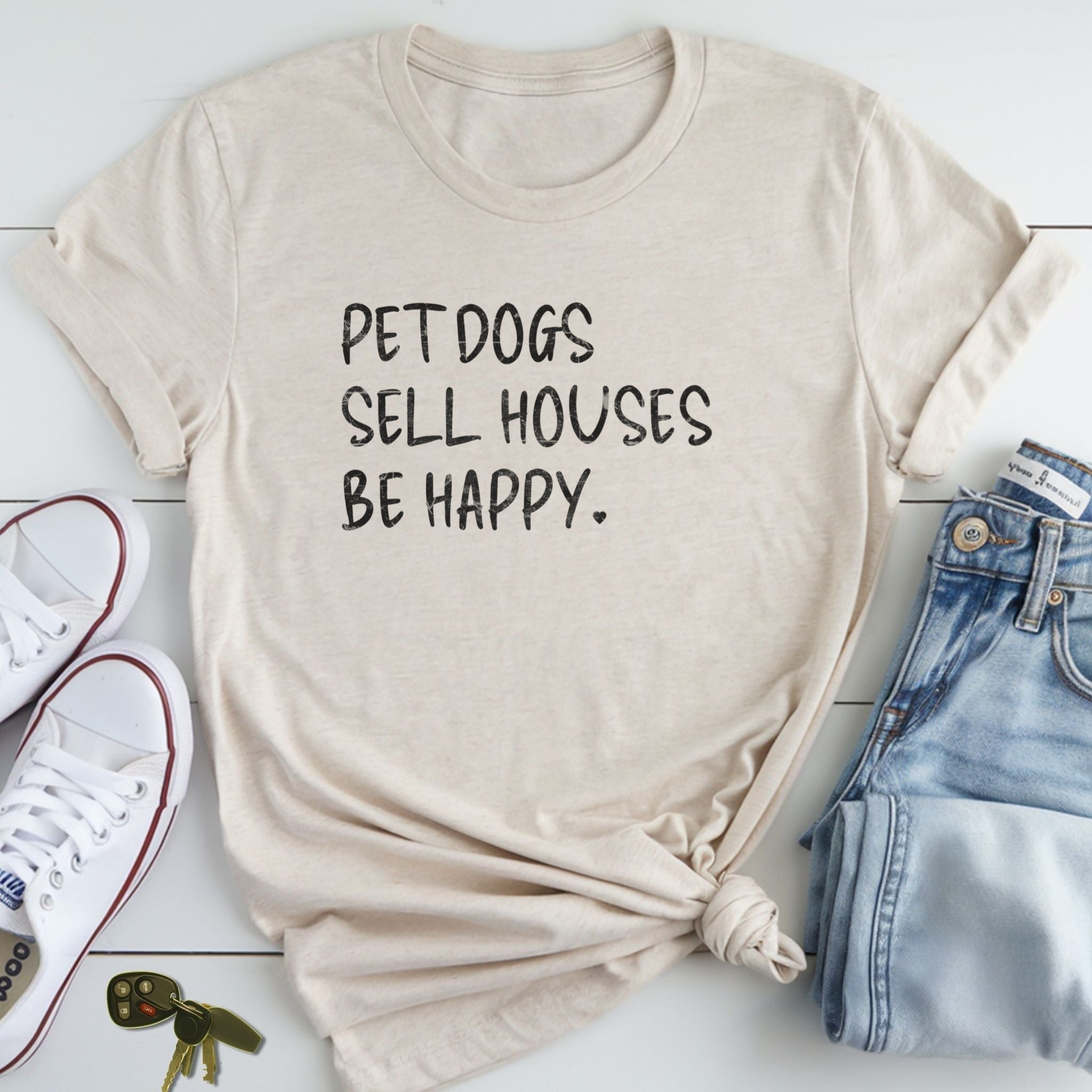A beige t-shirt with the text "PETDOGS SELL HOUSES BE HAPPY." printed on it, along with a pair of jeans and white sneakers.