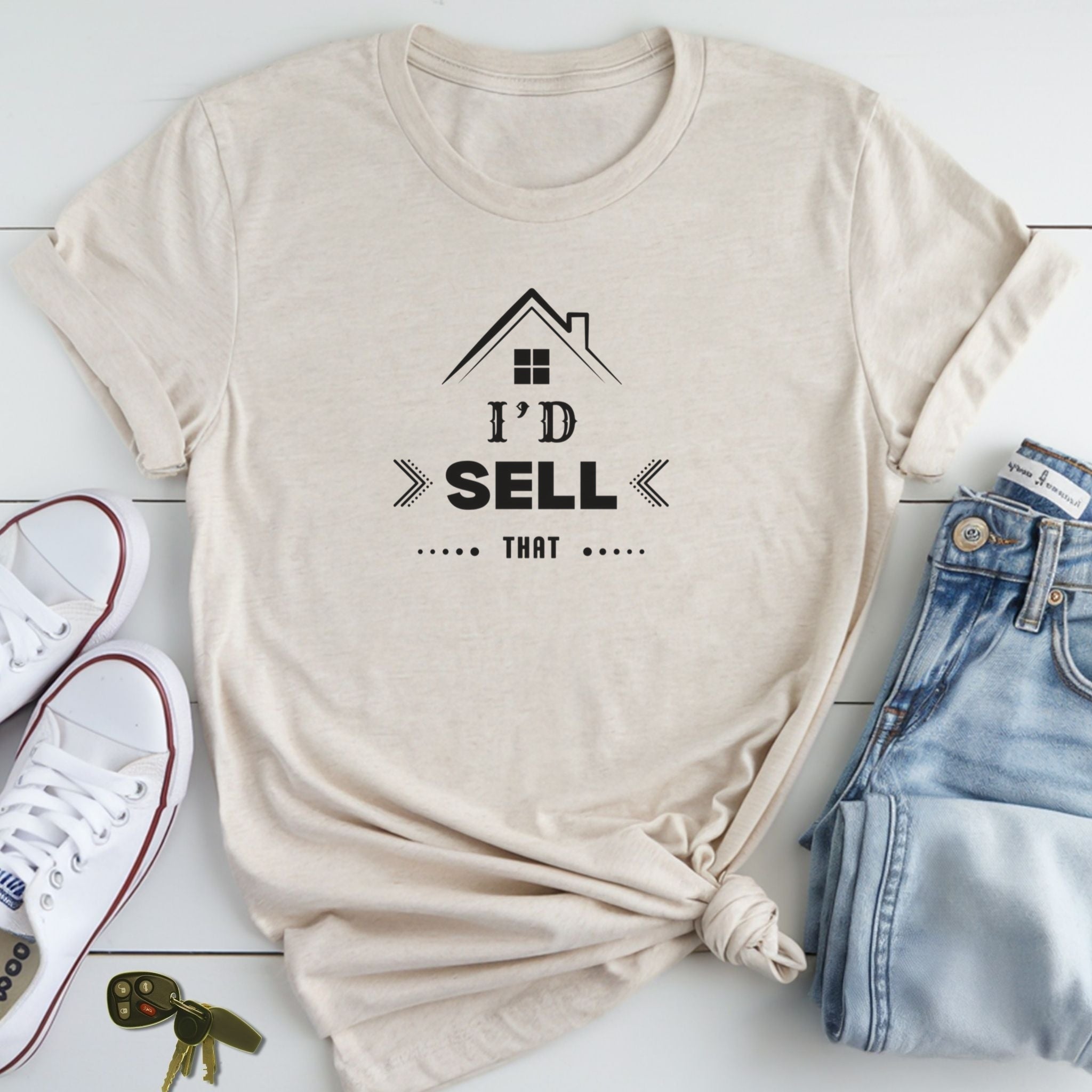 A beige t-shirt with a graphic design and text, along with a pair of jeans and sneakers, are laid out on a white surface.