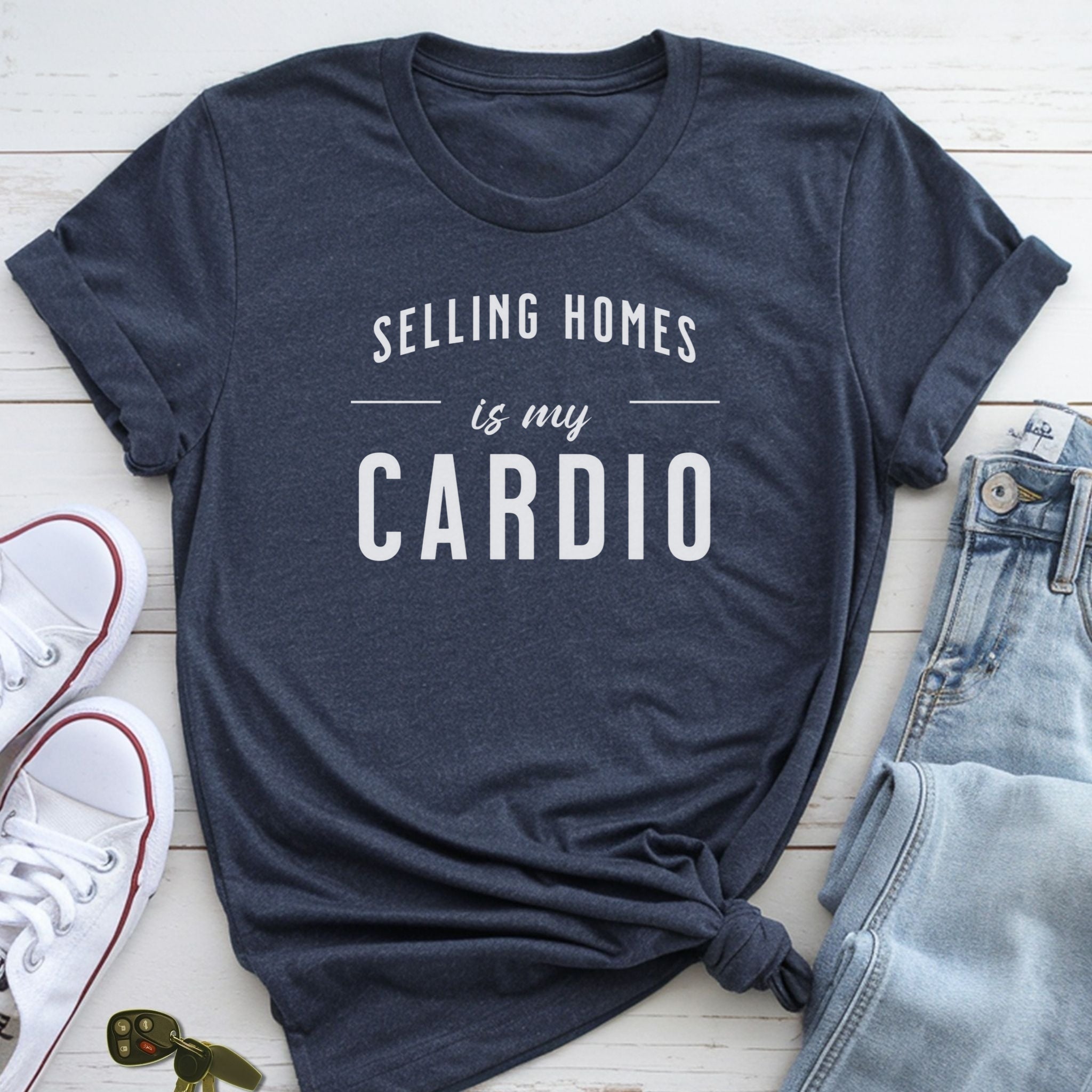 A navy blue t-shirt with the text "Selling Homes is my cardio" printed on it, along with a pair of jeans and white sneakers.
