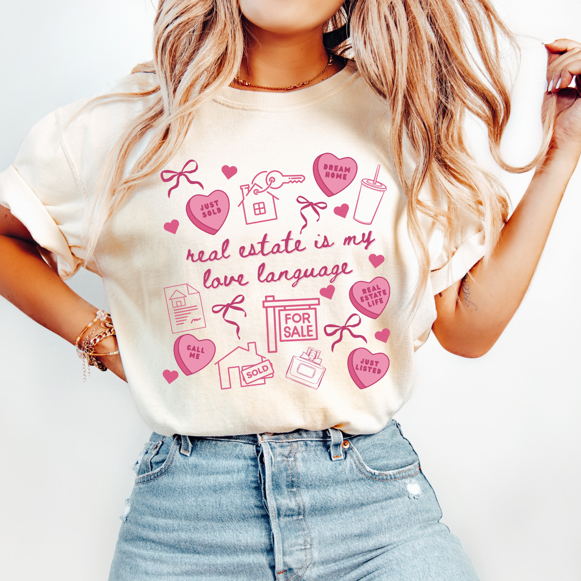 A woman wearing a white t-shirt with a graphic design printed on it, featuring various icons and text related to real estate and love.