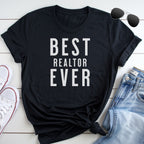 A black t-shirt with the text "BEST REALTOR EVER" printed on it, along with a pair of sunglasses and a pair of jeans.