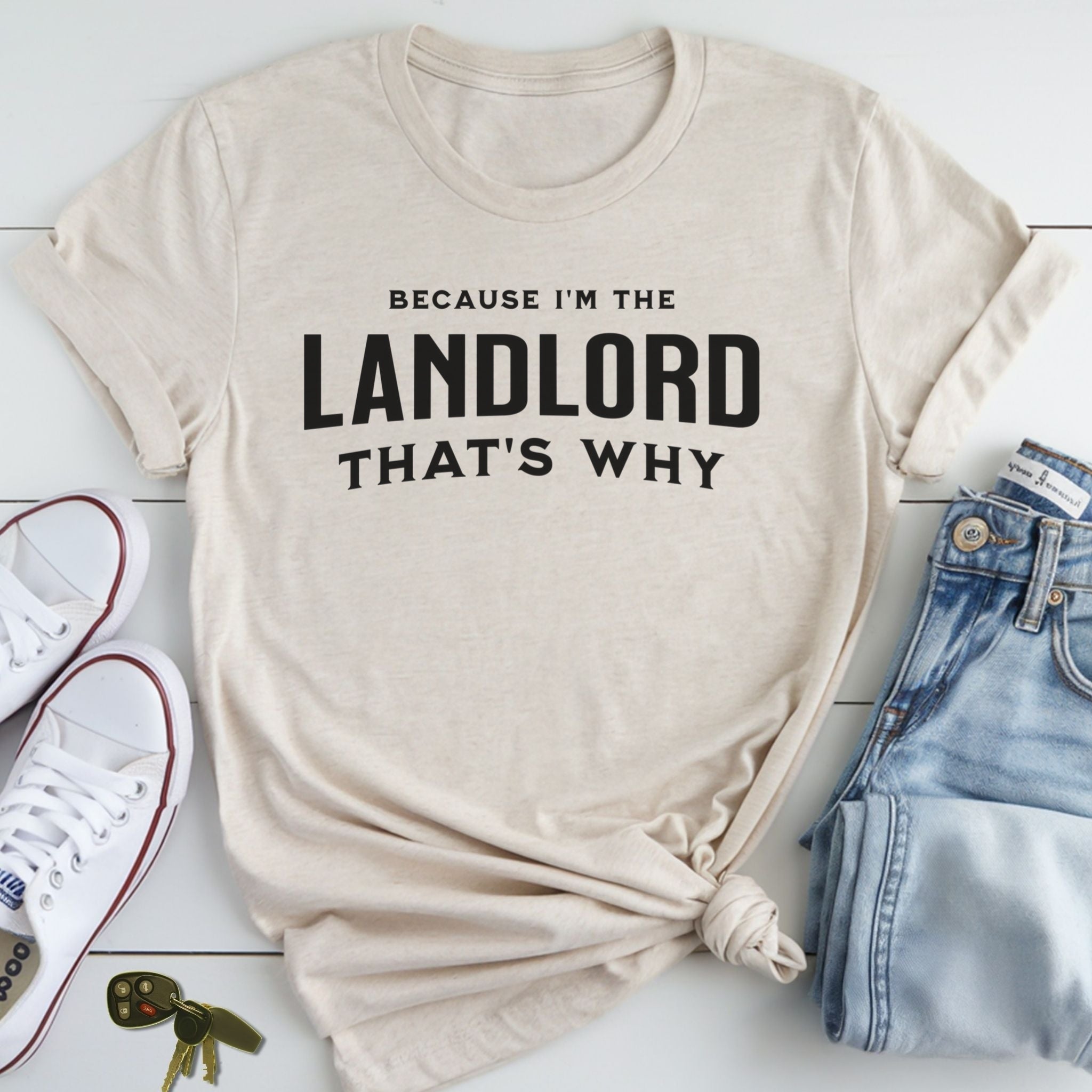 A beige t-shirt with the text "BECAUSE I'M THE LANDLORD THAT'S WHY" printed on it, along with a pair of jeans and a pair of white sneakers.
