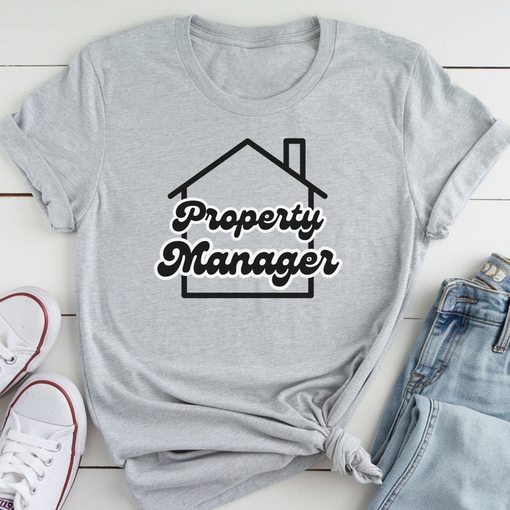 A gray t-shirt with the text "Property Manager" printed on it, along with a graphic of a house. The t-shirt is laid out on a white surface, and there are a pair of jeans and white sneakers visible in the background.