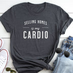 A gray t-shirt with the text "Selling Homes is my cardio" printed on it, along with a pair of jeans and sunglasses.