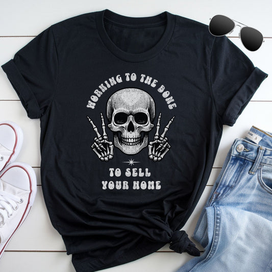 A black t-shirt with a skull graphic and text, along with a pair of jeans and sunglasses, laid out on a white surface.