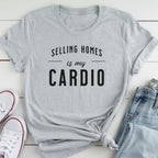 A gray t-shirt with the text "Selling homes is my cardio" printed on it, along with a pair of jeans and white sneakers.