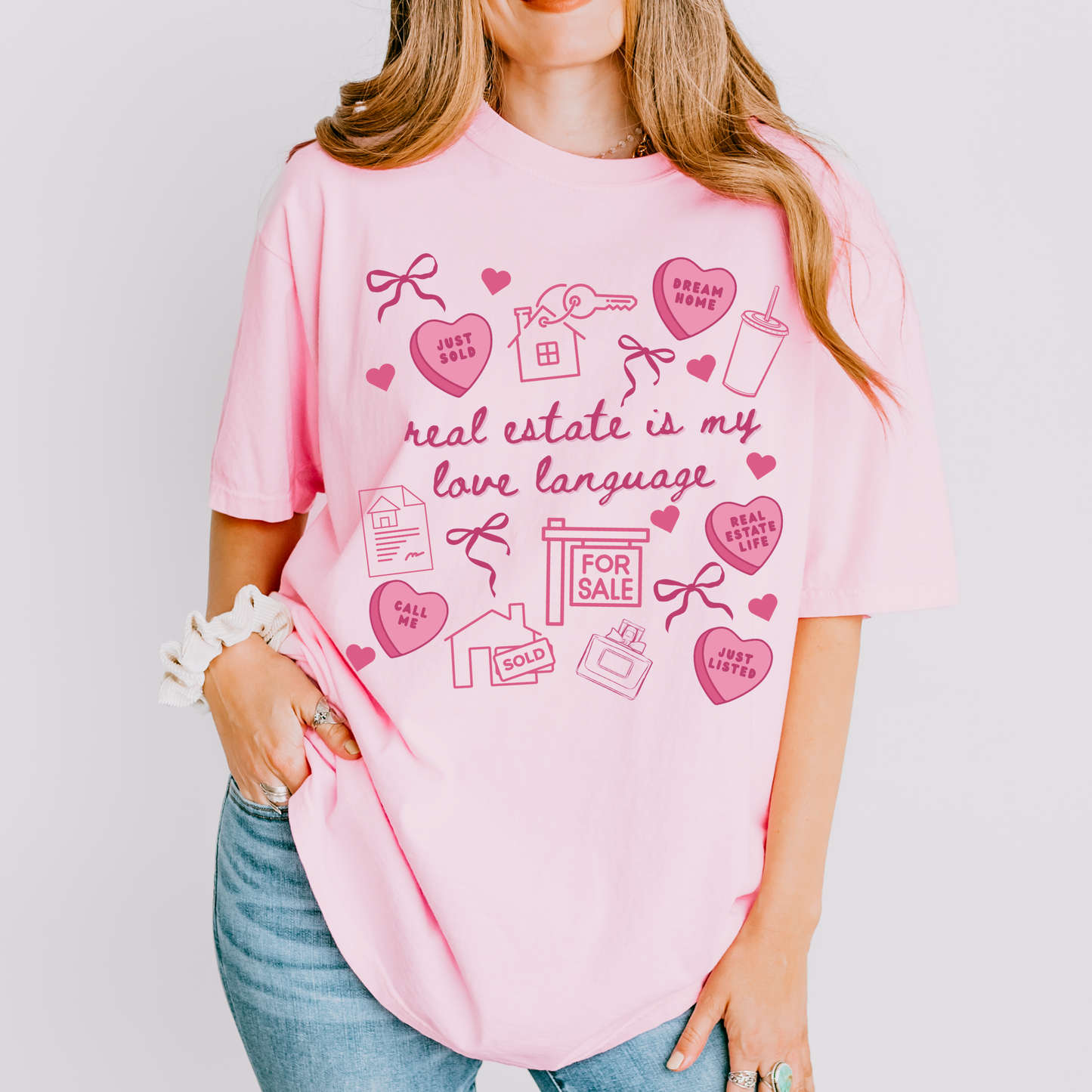 A woman wearing a pink t-shirt with a graphic design related to real estate, including a house, keys, and other symbols.