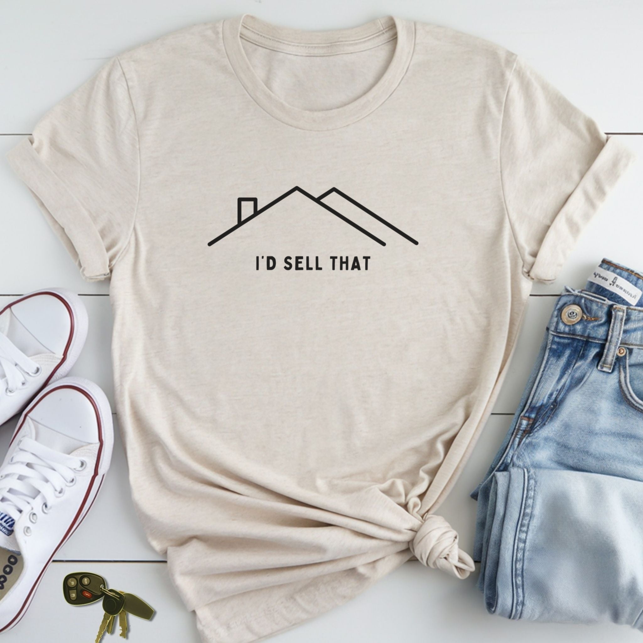 A beige t-shirt with a graphic design and text printed on it, along with a pair of jeans and sneakers, all laid out on a white surface.