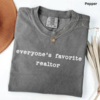 A gray t-shirt with the text "Everyone's favorite realtor" printed on it, along with a small pendant necklace.