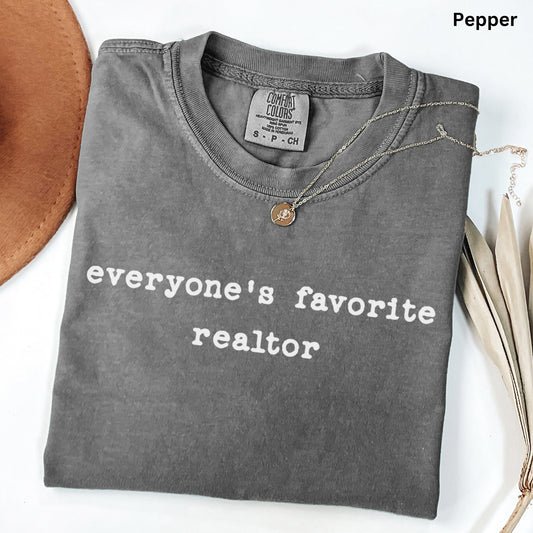 A gray t-shirt with the text "Everyone's favorite realtor" printed on it, along with a small pendant necklace.