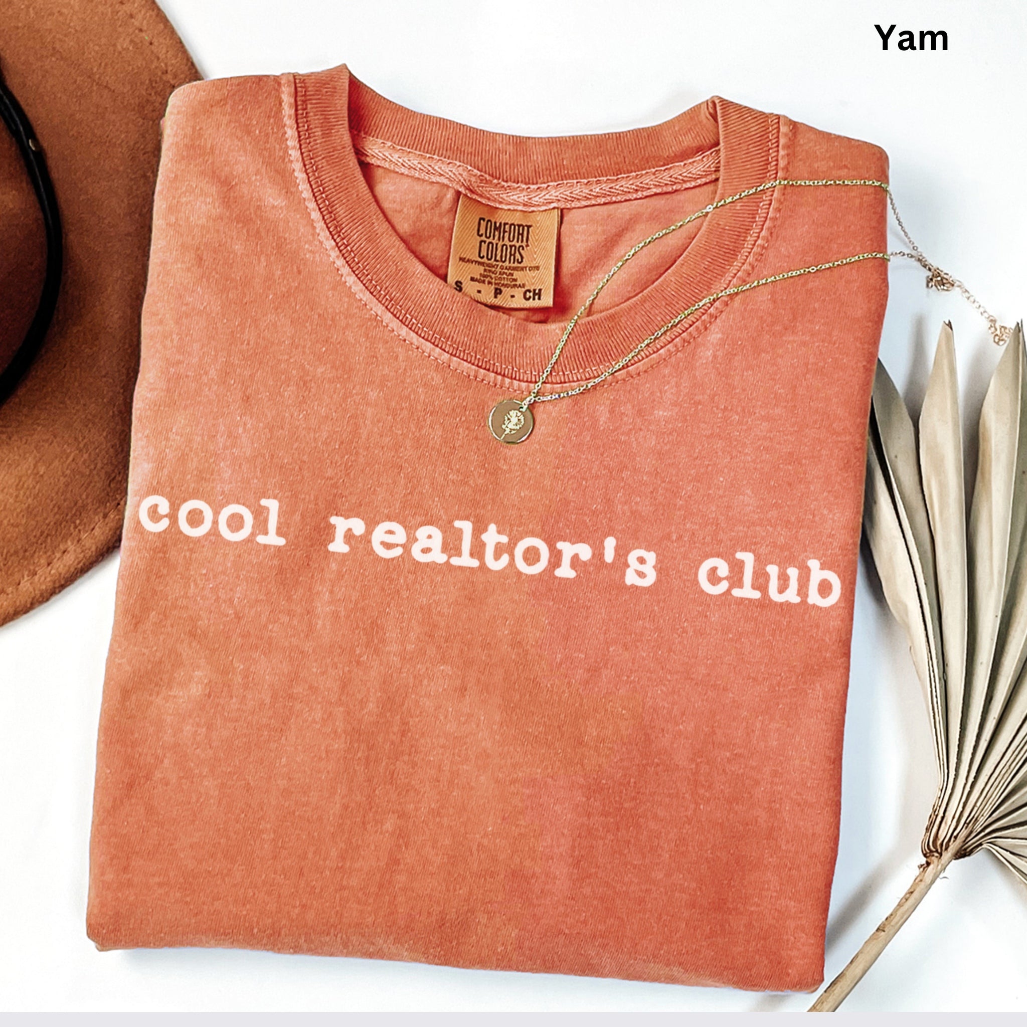 A red t-shirt with the text "cool realtor's club" printed on it, along with a gold necklace and a brown hat.