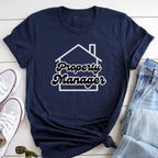 A navy blue t-shirt with the text "Property Manager" printed on it, along with a graphic of a house. The t-shirt is laid out on a white surface, with a pair of jeans and white sneakers visible next to it.