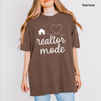 A woman wearing a brown t-shirt with the text "realtor mode" printed on it, along with a heart and house symbol.