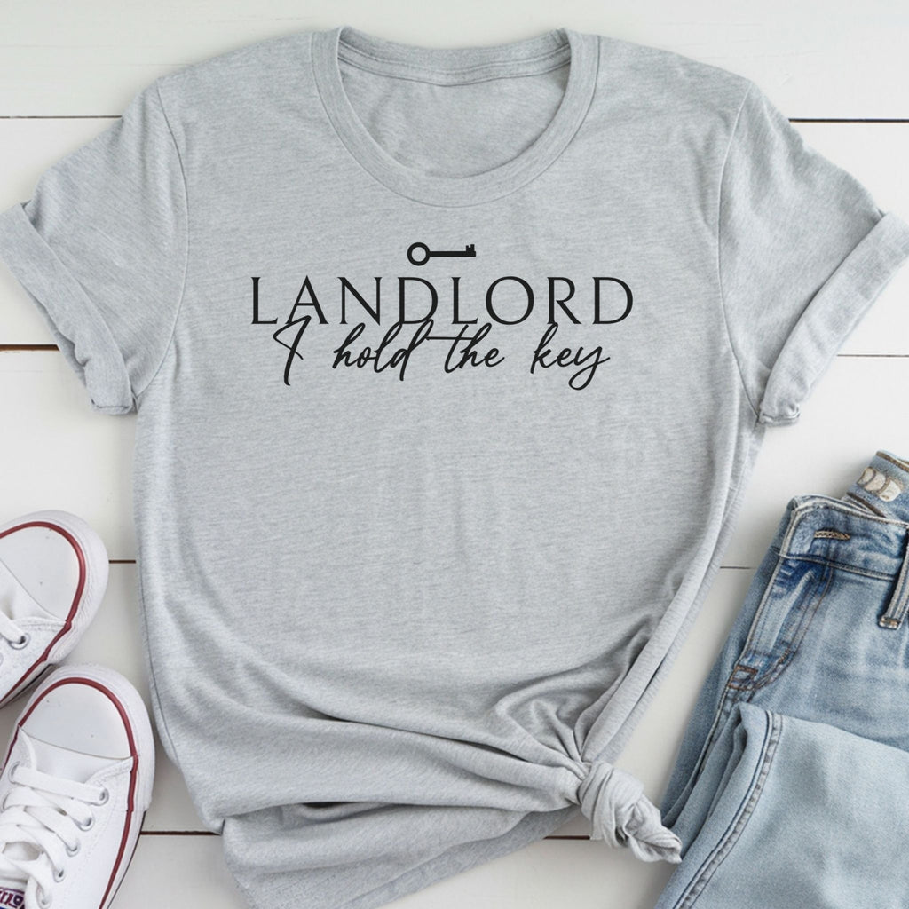 A gray t-shirt with the text "LANDLORD I hold the key" printed on it, along with a key symbol. The t-shirt is laid out on a white surface, and there are a pair of jeans and white sneakers visible in the image.