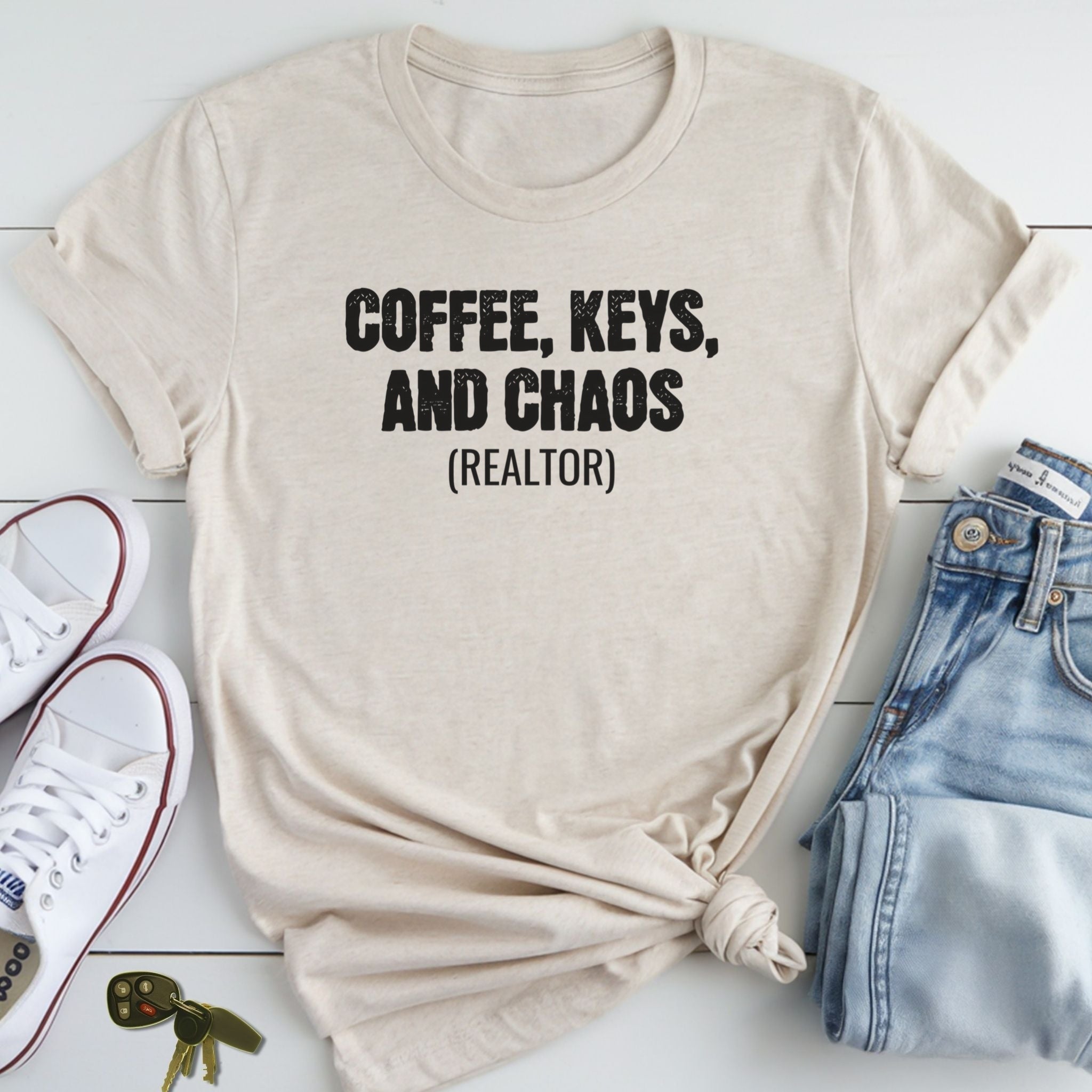 A beige t-shirt with the text "COFFEE, KEYS, AND CHAOS (REALTOR)" printed on it, along with a pair of jeans and a pair of white sneakers.