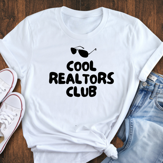 A white t-shirt with the text "COOL REALTORS CLUB" printed on it, along with sunglasses and a casual outfit consisting of jeans and white sneakers.