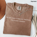 a brown t-shirt with a humorous text printed on it, along with a necklace and some leaves.
