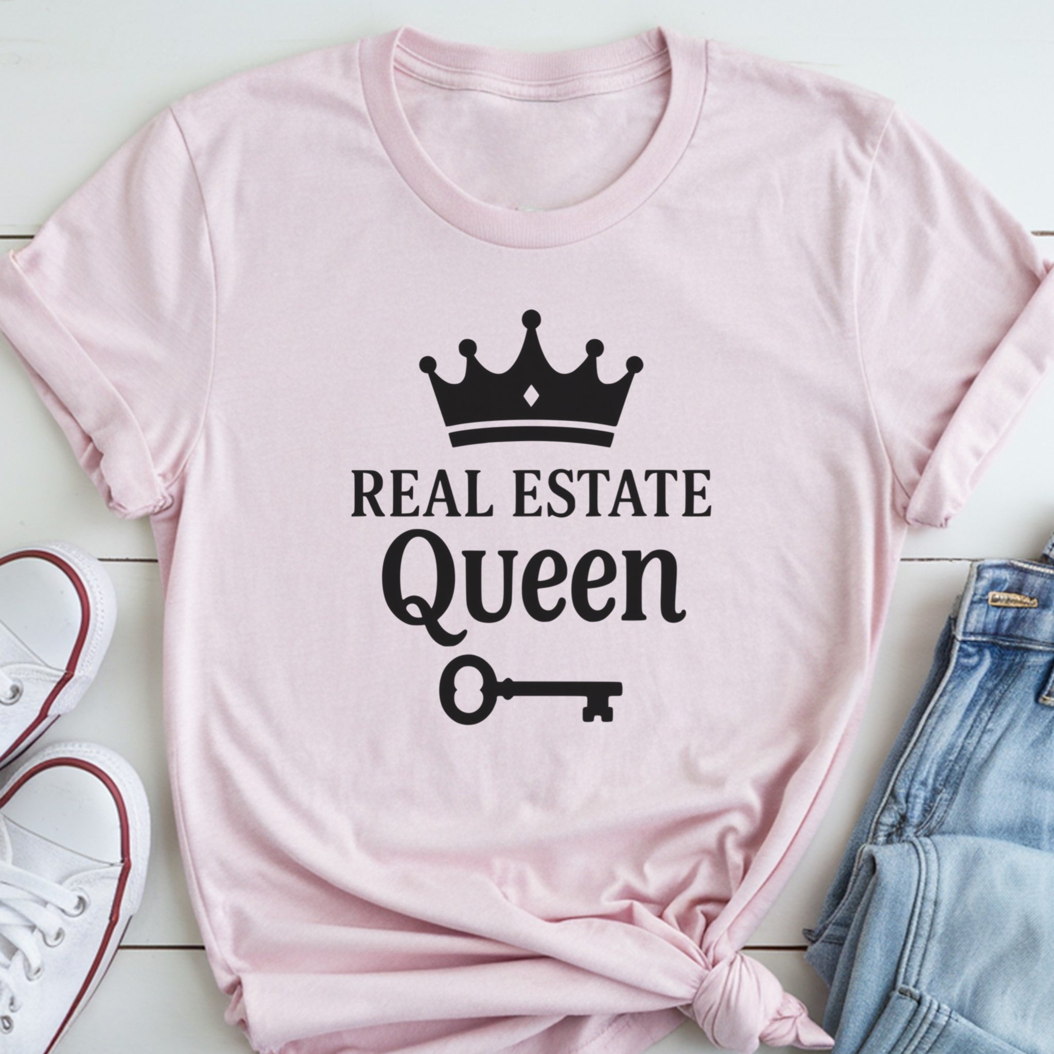A pink t-shirt with the text "REAL ESTATE QUEEN" printed on it, along with a crown and a key symbol.