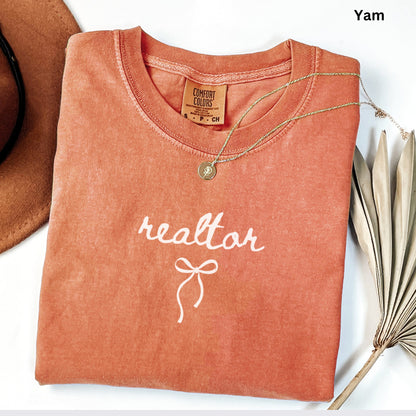 a red t-shirt with the word "realtor" printed on it, along with a gold necklace and a brown hat.