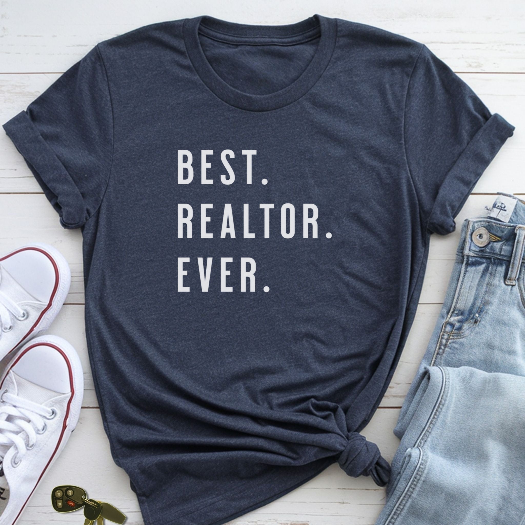A navy blue t-shirt with the text "BEST. REALTOR. EVER." printed on it, along with a pair of jeans and white sneakers.