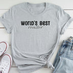 A gray t-shirt with the text "WORLD'S BEST REALTOR" printed on it, along with a pair of jeans and white sneakers.