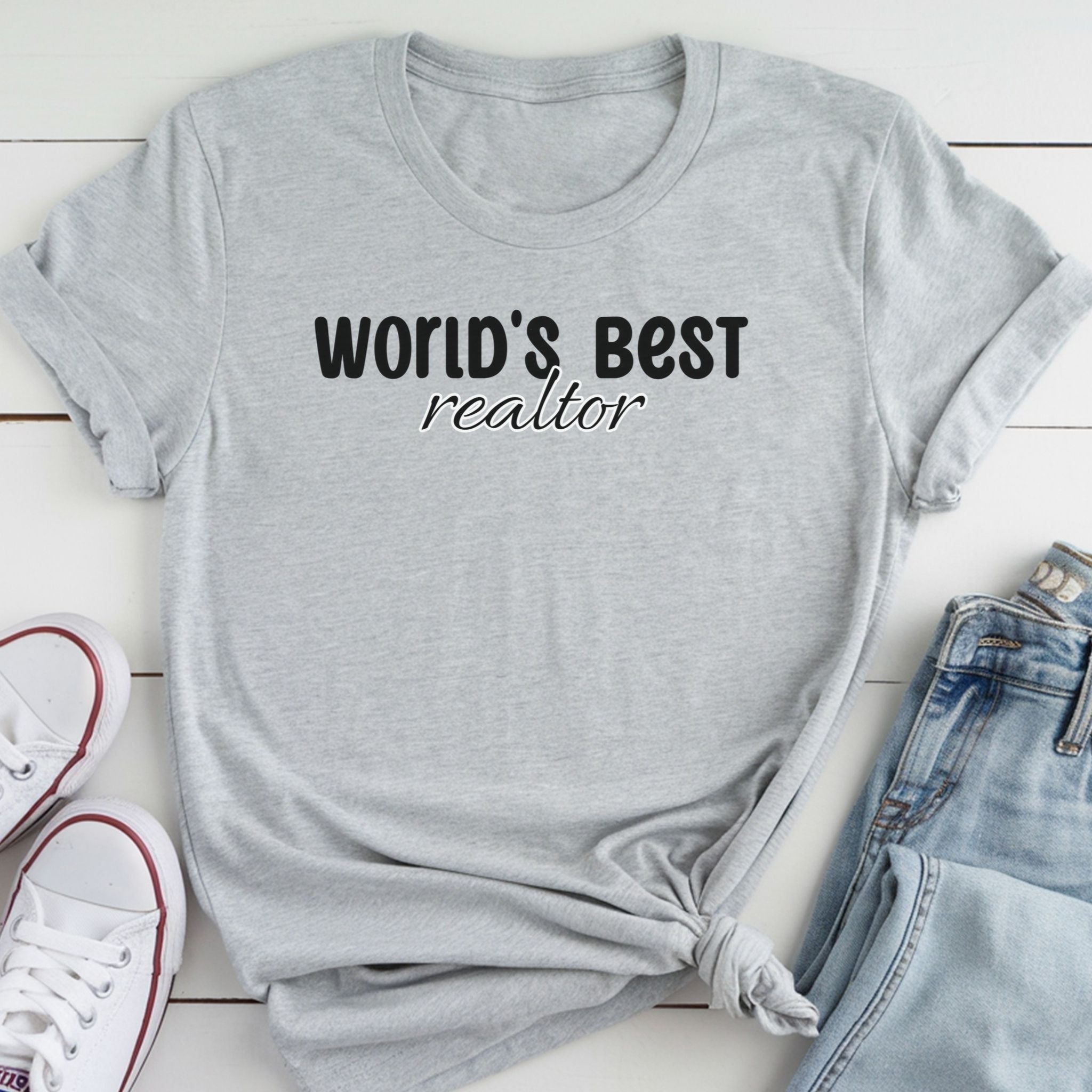 A gray t-shirt with the text "WORLD'S BEST REALTOR" printed on it, along with a pair of jeans and white sneakers.