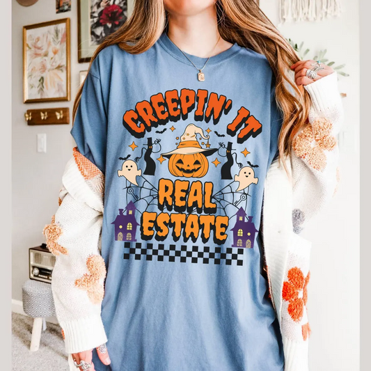 A woman wearing a blue t-shirt with a Halloween-themed graphic design, including a jack-o-lantern, bats, and a house.