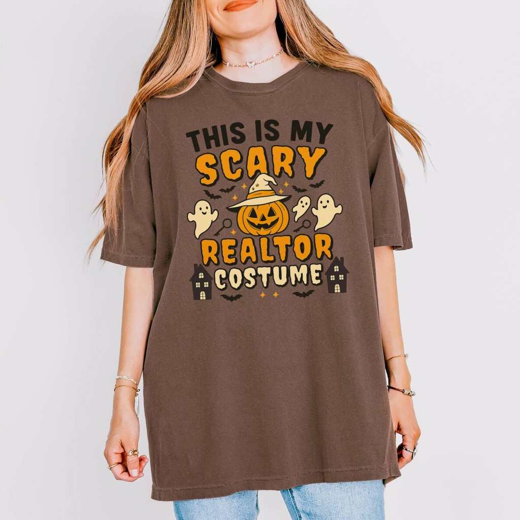 A woman wearing a brown t-shirt with a Halloween-themed design, including a jack-o-lantern, ghost, and houses.