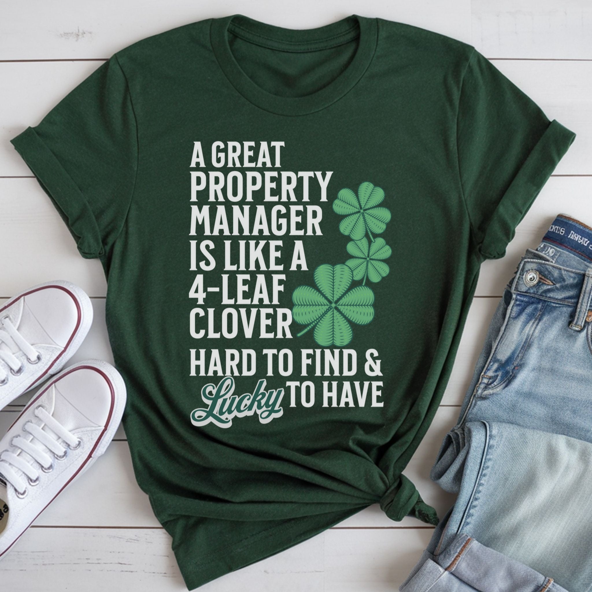 A green t-shirt with white text and a clover graphic, along with a pair of jeans and white sneakers, all laid out on a white surface.