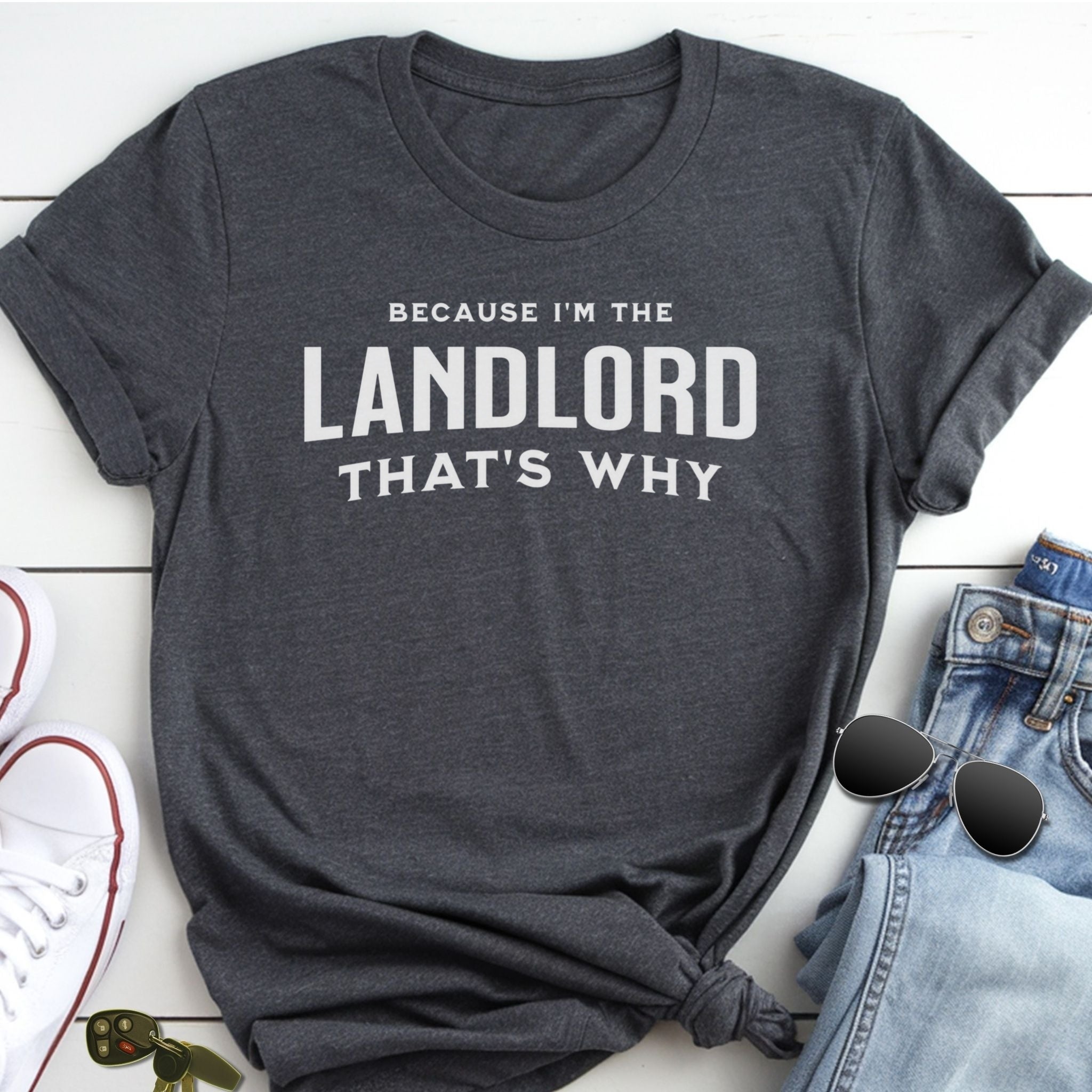 A gray t-shirt with the text "BECAUSE I'M THE LANDLORD THAT'S WHY" printed on it, along with a pair of jeans and sunglasses.