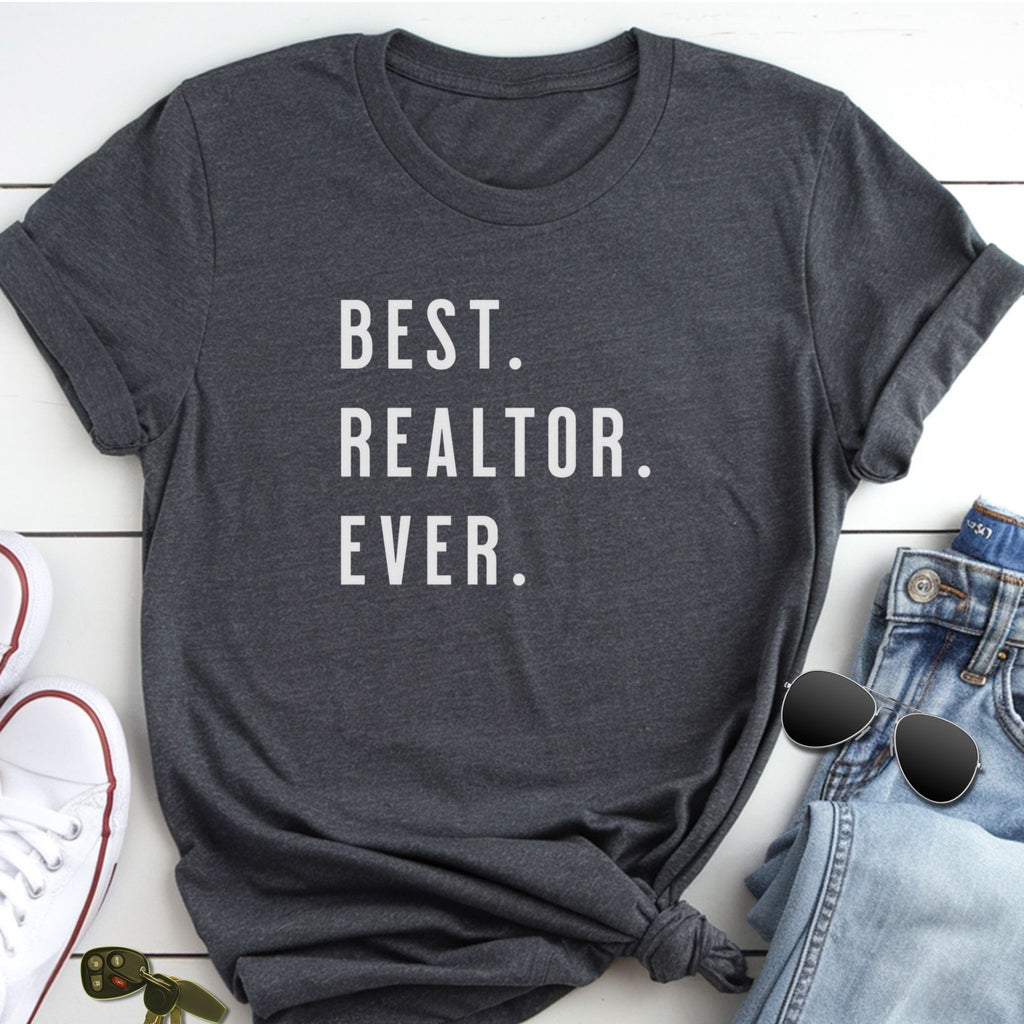 A gray t-shirt with the text "BEST. REALTOR. EVER." printed on it, along with a pair of jeans and sunglasses.