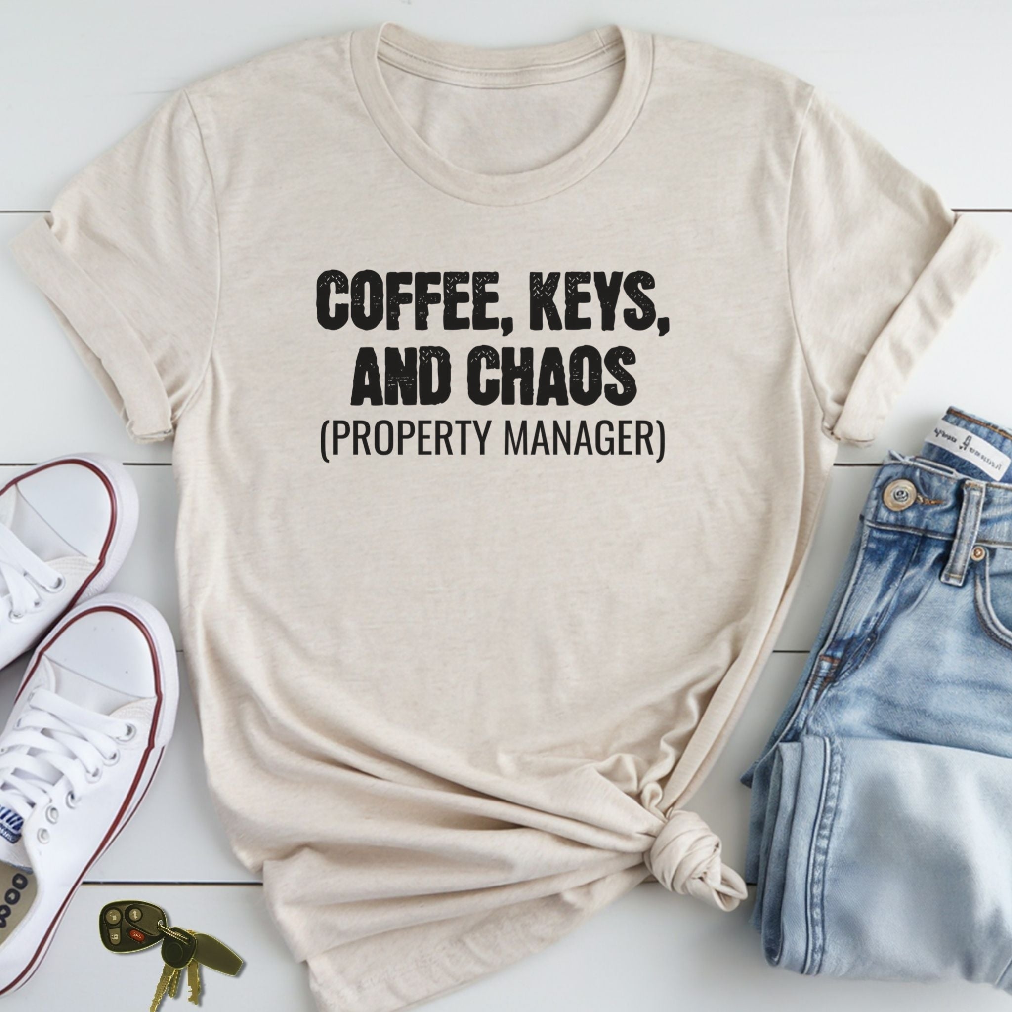 A beige t-shirt with the text "COFFEE, KEYS, AND CHAOS (PROPERTY MANAGER)" printed on it, along with a pair of jeans and a pair of white sneakers.