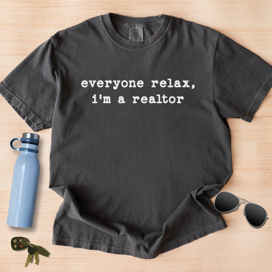 a gray t-shirt with the text "everyone relax, I'm a realtor" printed on it, along with a pair of sunglasses, a water bottle, and keys.