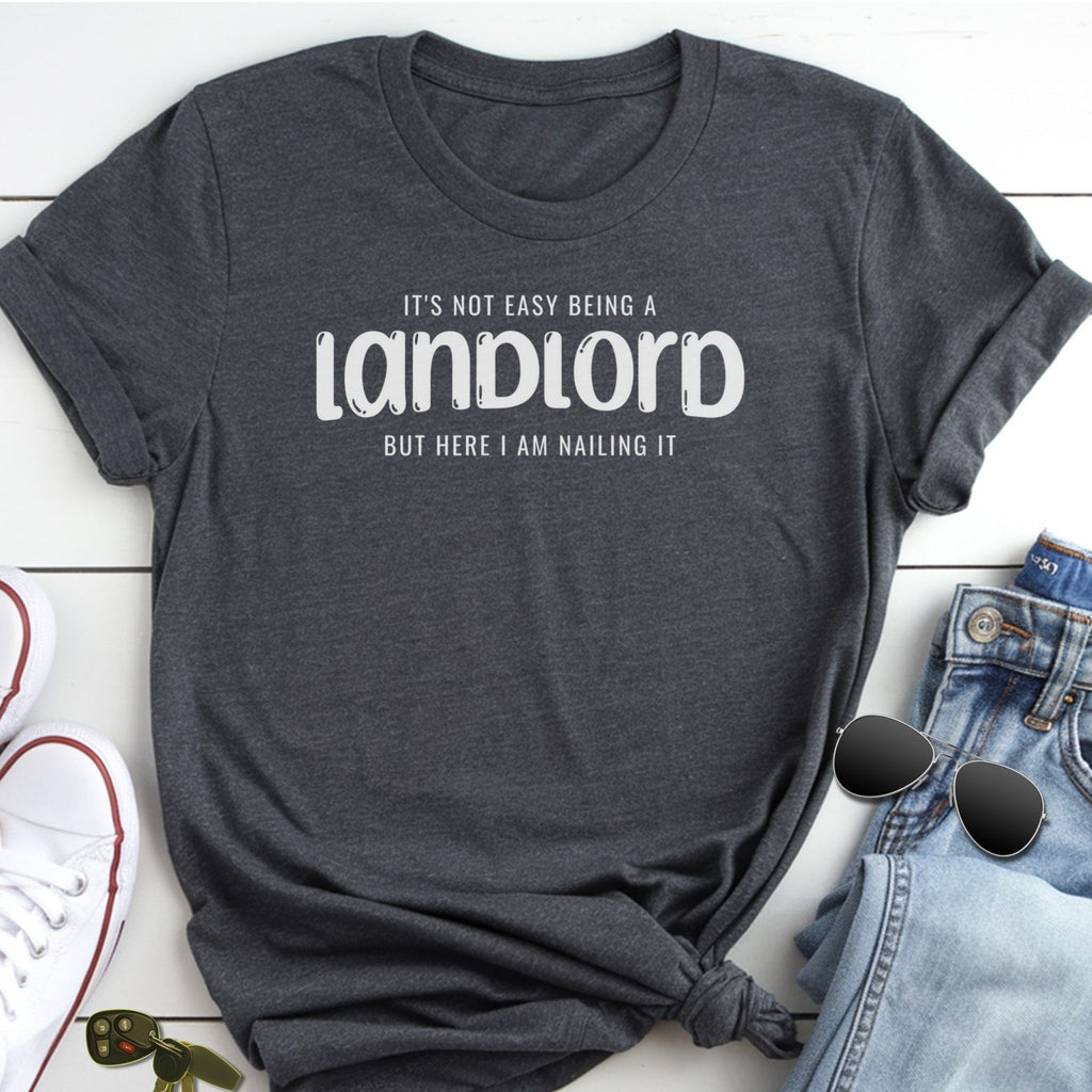 A gray t-shirt with the text "IT'S NOT EASY BEING A LANDLORD BUT HERE I AM MAKING IT" printed on it, along with a pair of jeans and sunglasses.