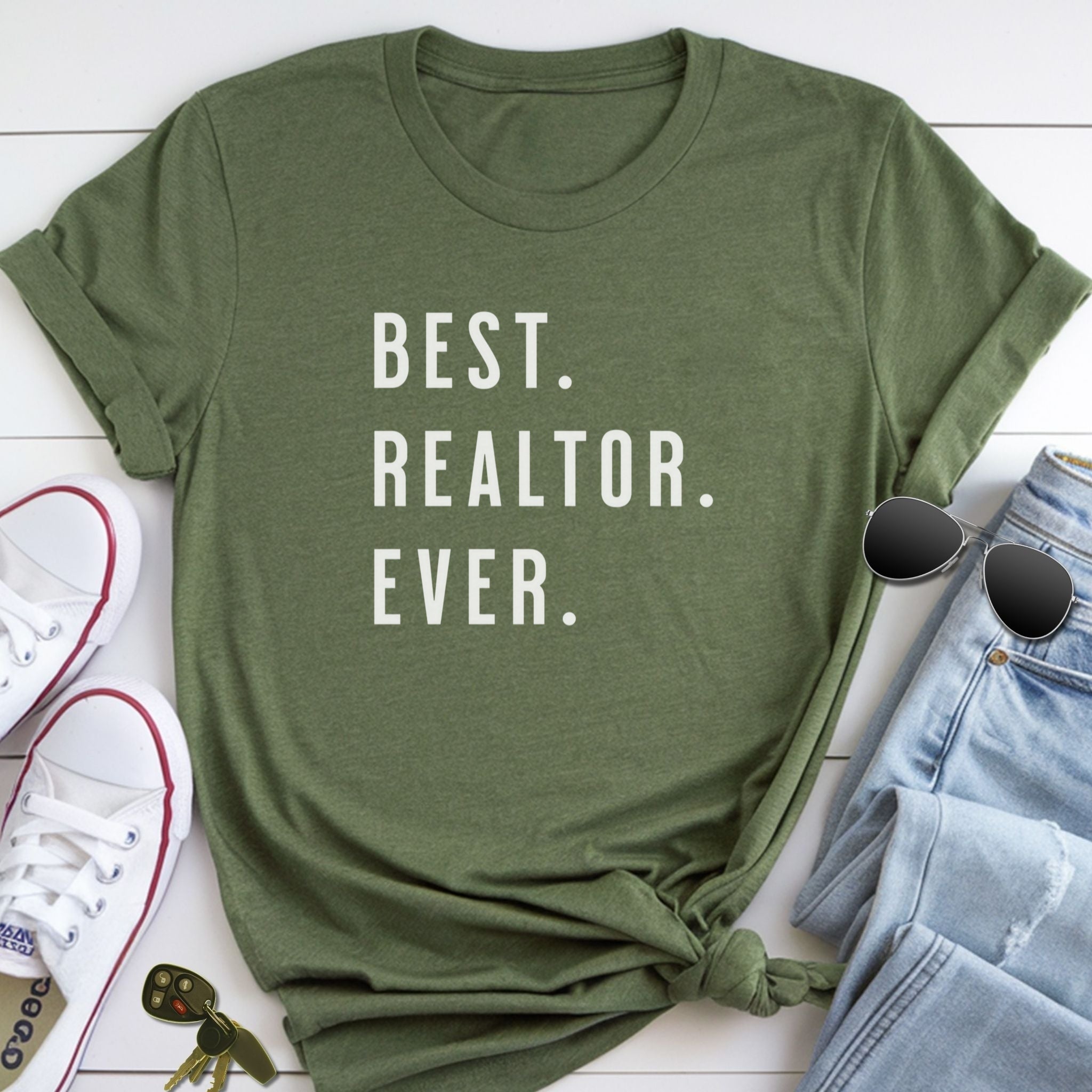 A green t-shirt with the text "BEST REALTOR. EVER." printed on it, along with a pair of sunglasses, a pair of sneakers, and a keychain.