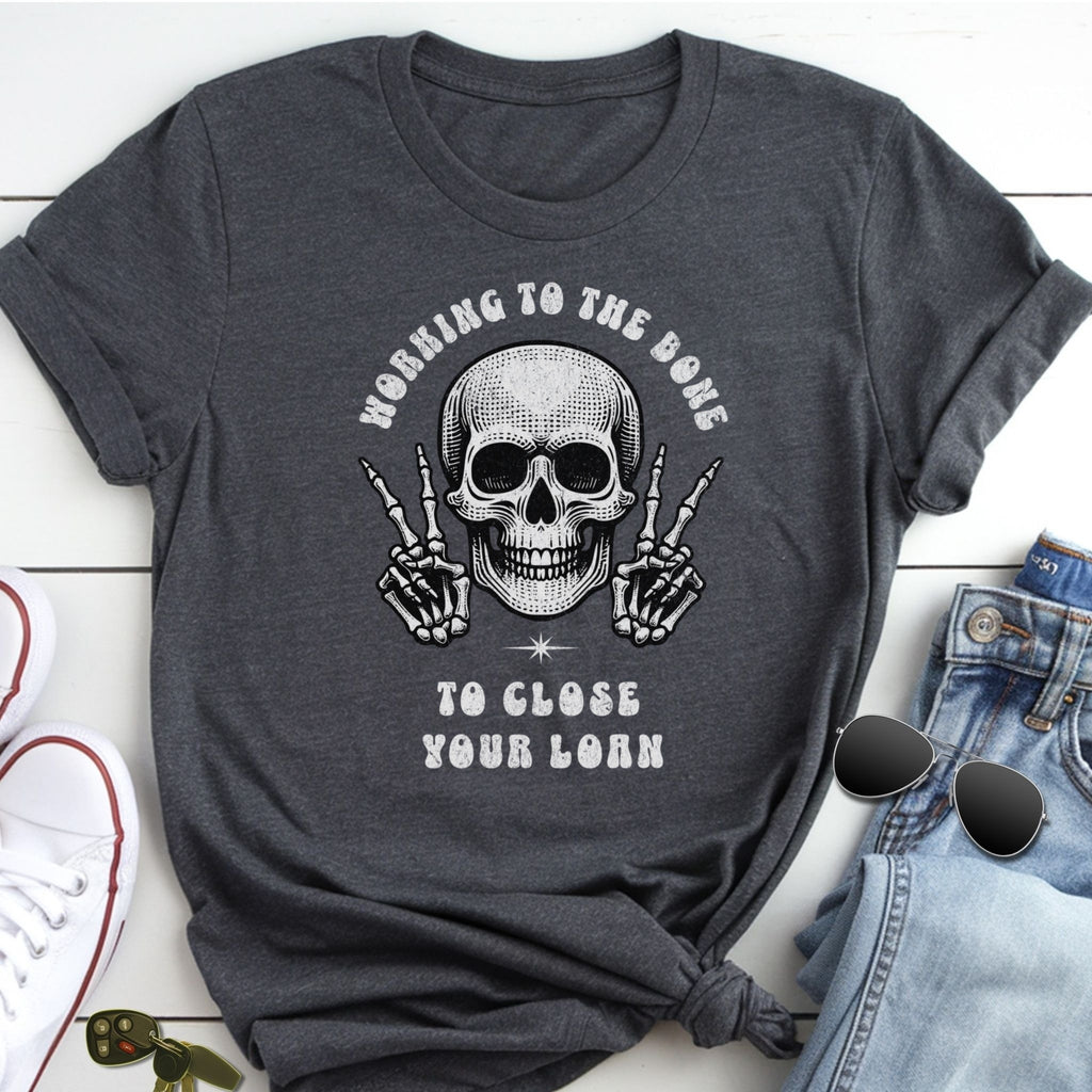 A gray t-shirt with a skull graphic and the text "Working to the bone to close your lone" printed on it, along with a pair of jeans and sunglasses.
