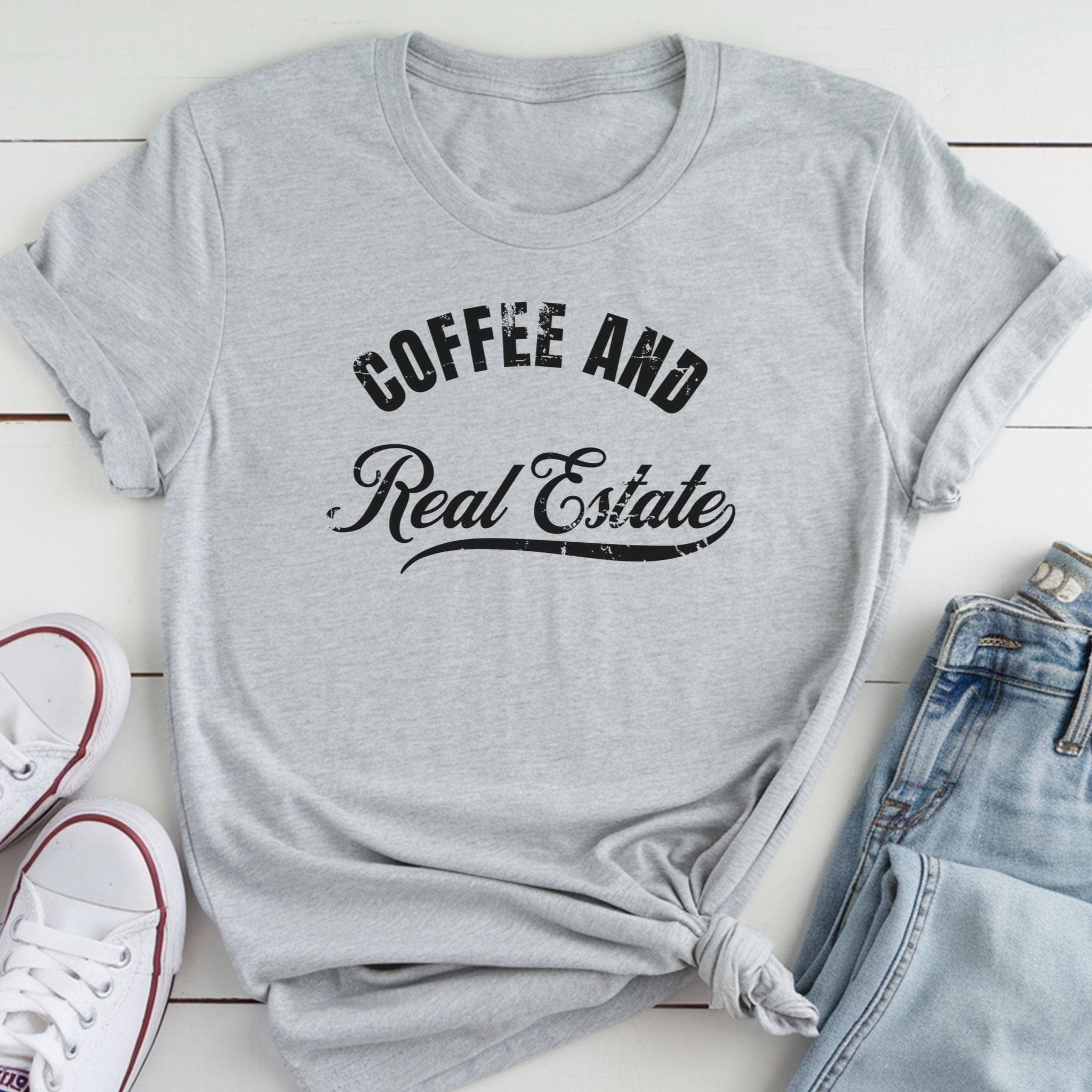 A gray t-shirt with the text "COFFEE AND REAL ESTATE" printed on it, along with a pair of jeans and white sneakers.