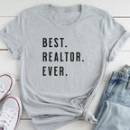 A gray t-shirt with the text "BEST. REALTOR. EVER." printed on it, along with a pair of jeans and white sneakers.