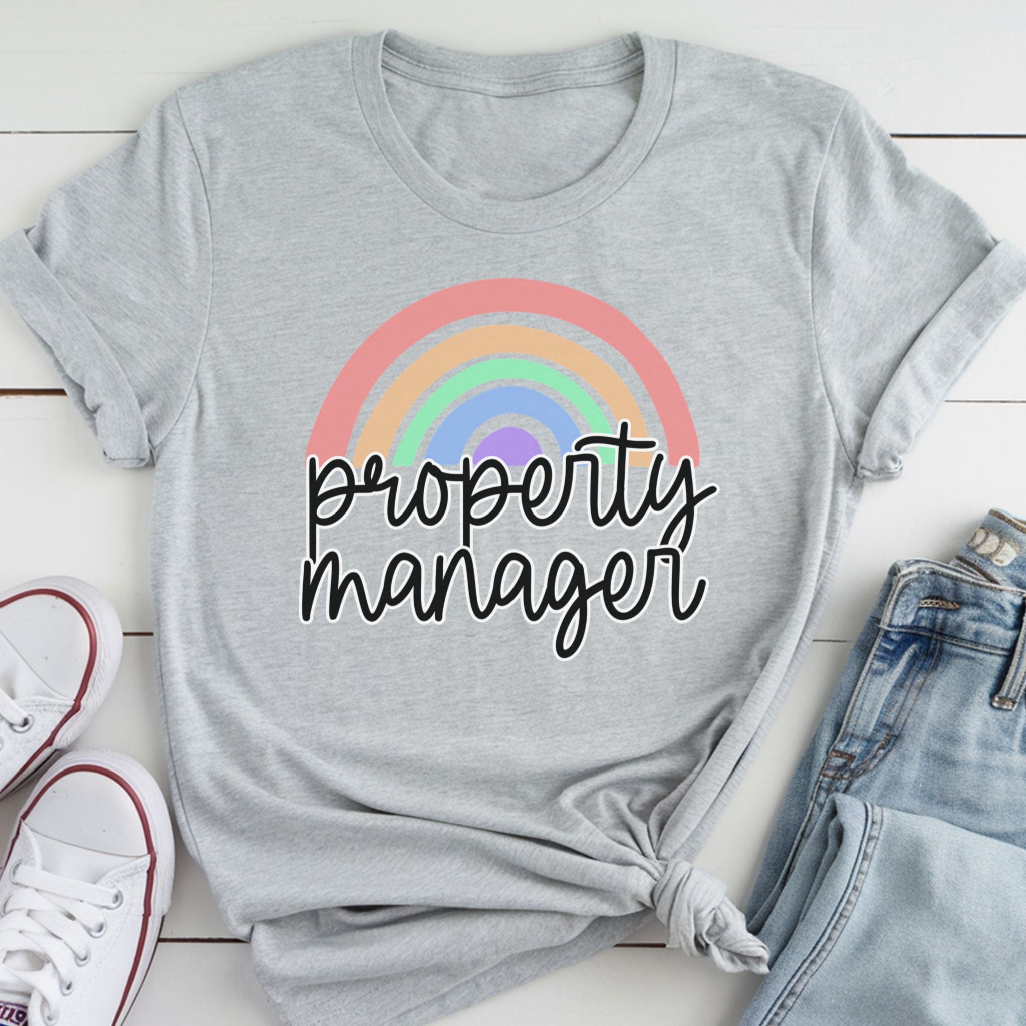 A gray t-shirt with a rainbow graphic and the text "Property Manager" printed on it, along with a pair of jeans and white sneakers.