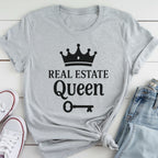 A gray t-shirt with the text "REAL ESTATE QUEEN" printed on it, along with a crown icon and a key symbol.