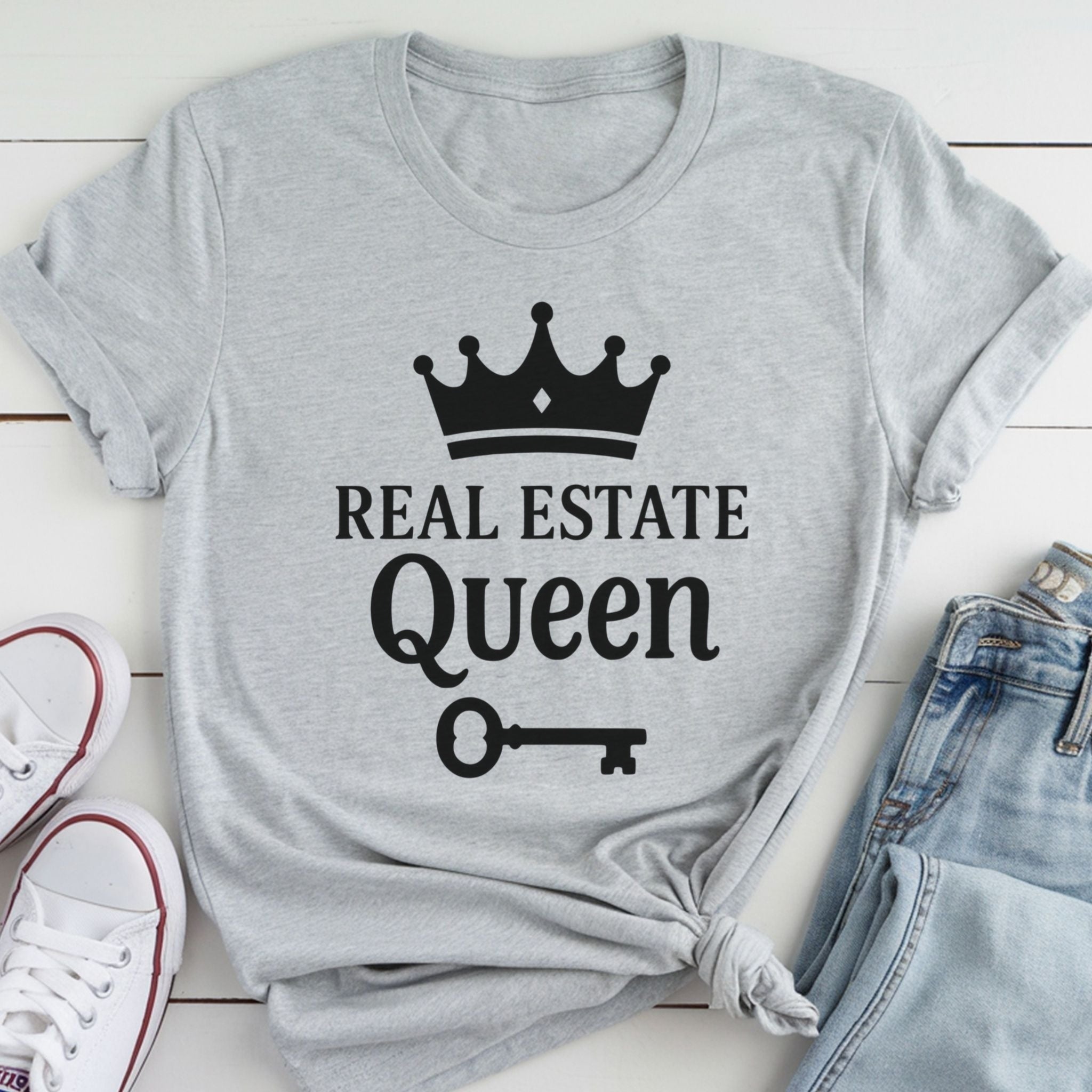 A gray t-shirt with the text "REAL ESTATE QUEEN" printed on it, along with a crown icon and a key symbol.