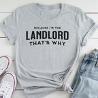 A gray t-shirt with the text "BECAUSE I'M THE LANDLORD THAT'S WHY" printed on it, along with a pair of jeans and white sneakers.