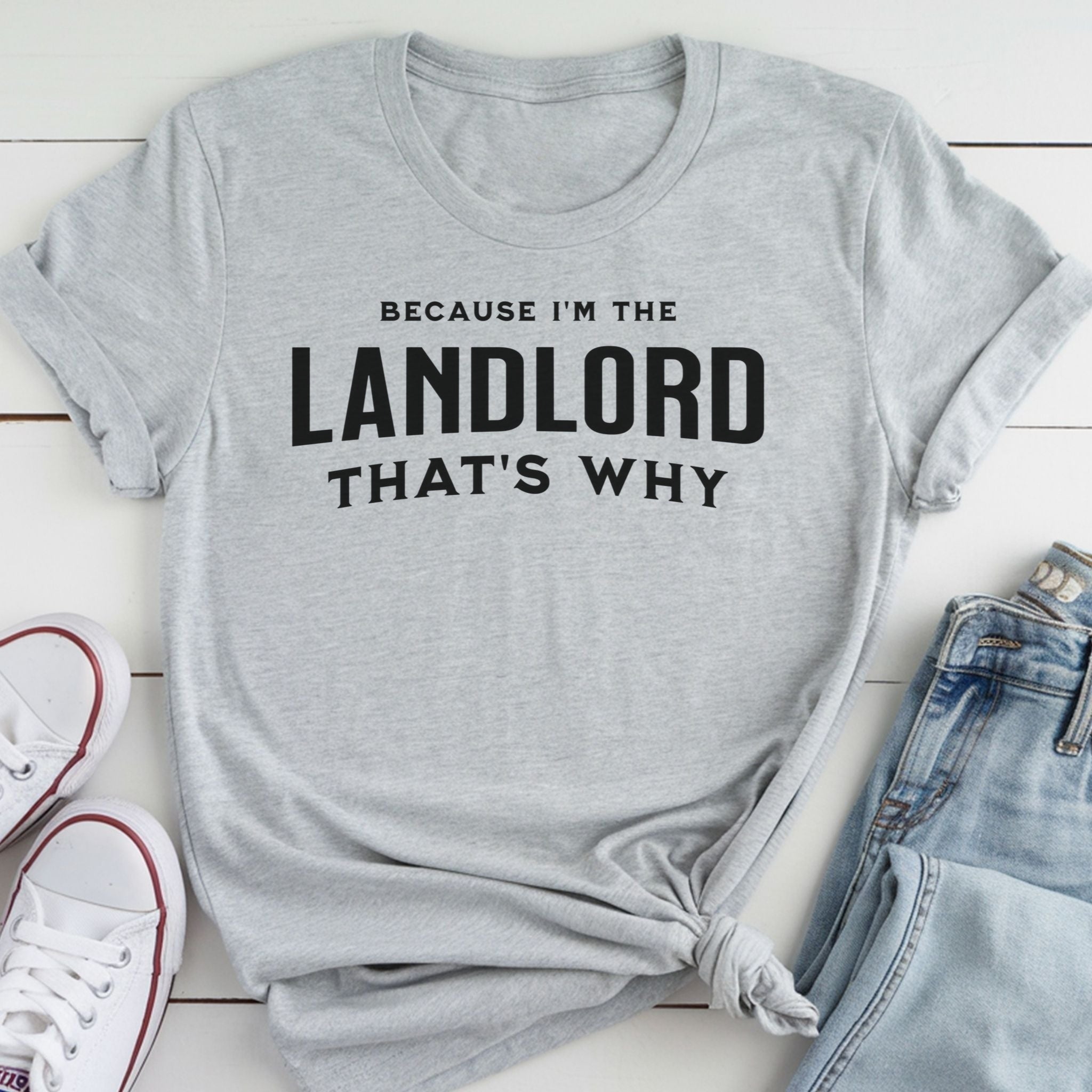A gray t-shirt with the text "BECAUSE I'M THE LANDLORD THAT'S WHY" printed on it, along with a pair of jeans and white sneakers.