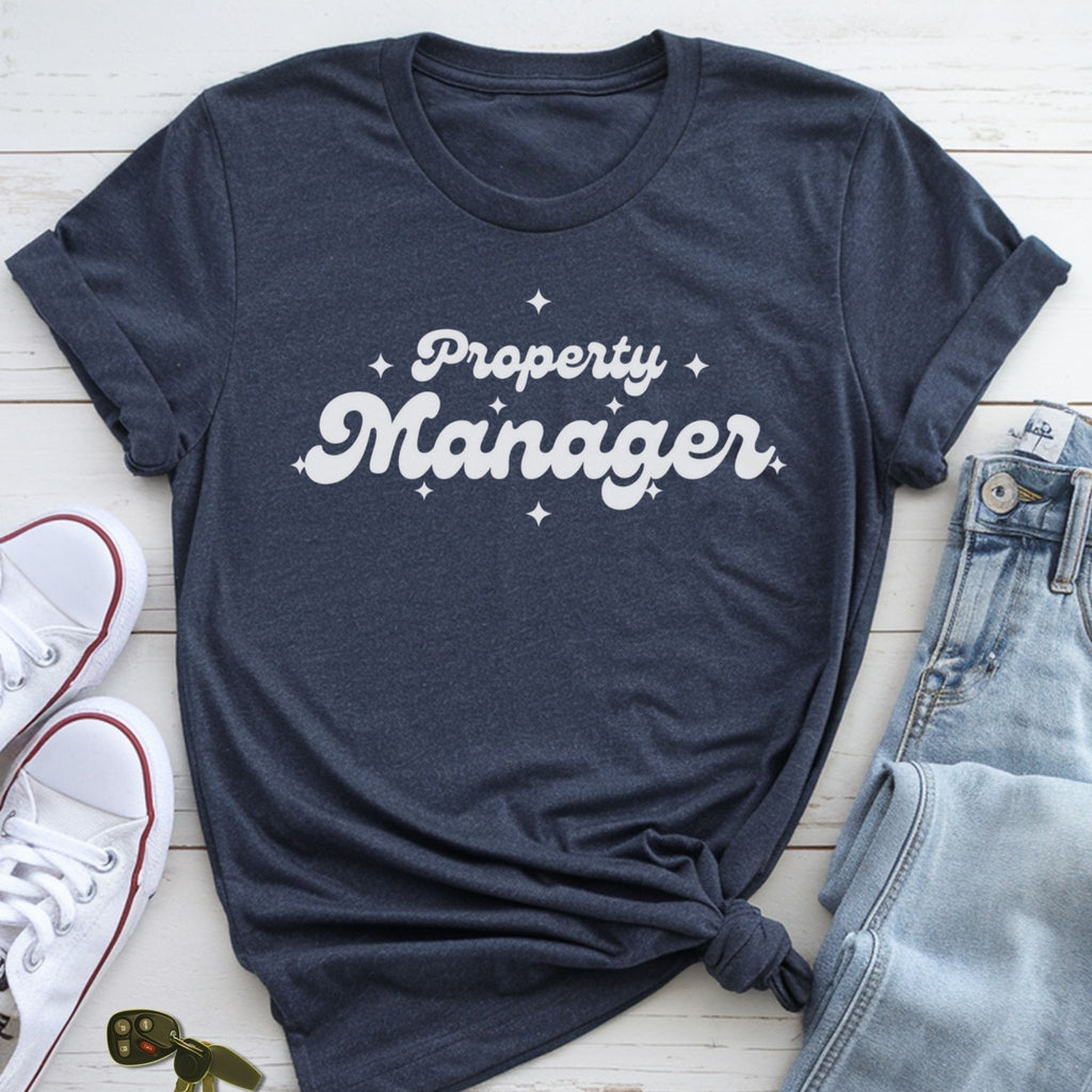 A navy blue t-shirt with the text "Property Manager" printed on it, along with some jeans and white sneakers, all laid out on a wooden surface.