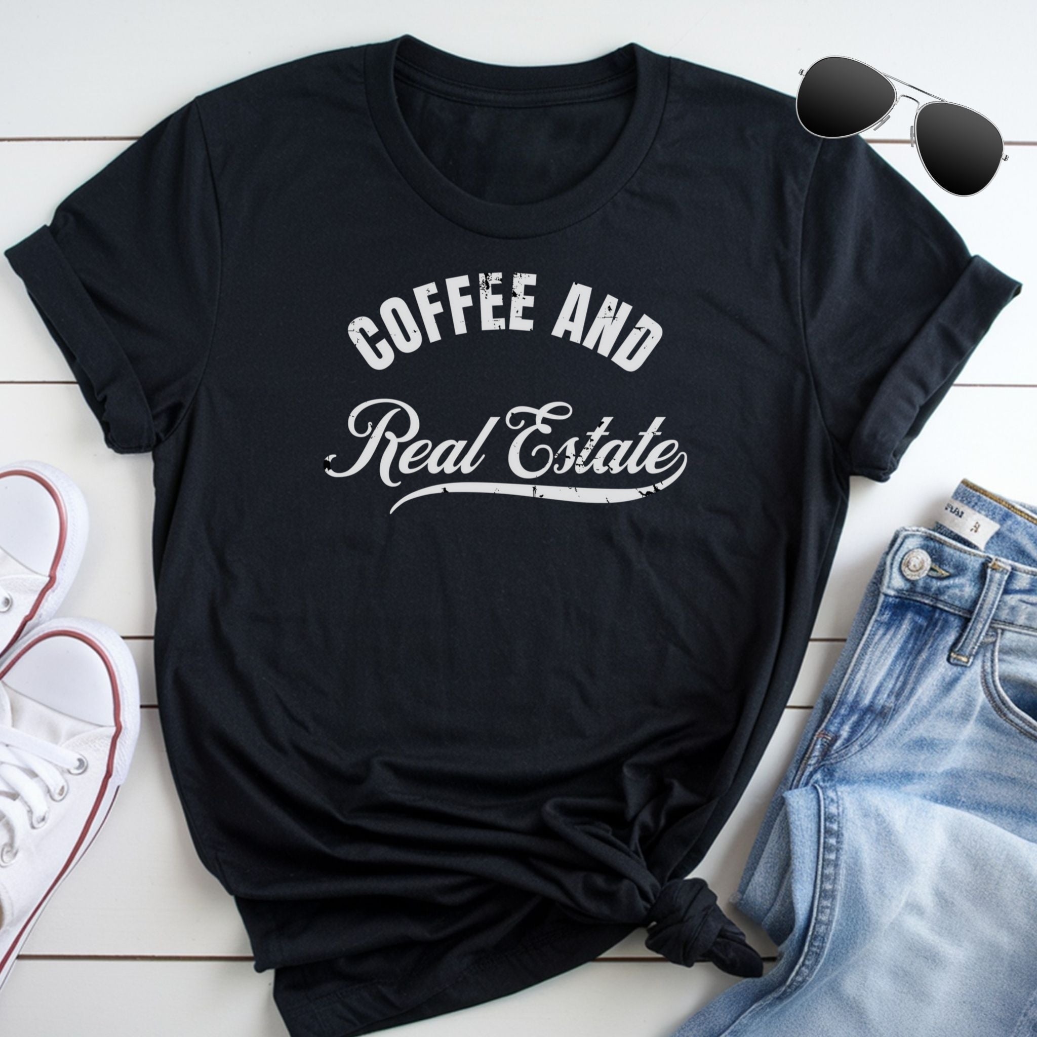 A black t-shirt with the text "COFFEE AND REAL ESTATE" printed on it, along with a pair of sunglasses and a pair of jeans.