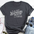 A gray t-shirt with white text that says "I AM THAT LEGENDARY REALTOR EVERYONE KEEPS TALKING ABOUT" is displayed on a white surface, accompanied by a pair of jeans and sunglasses.