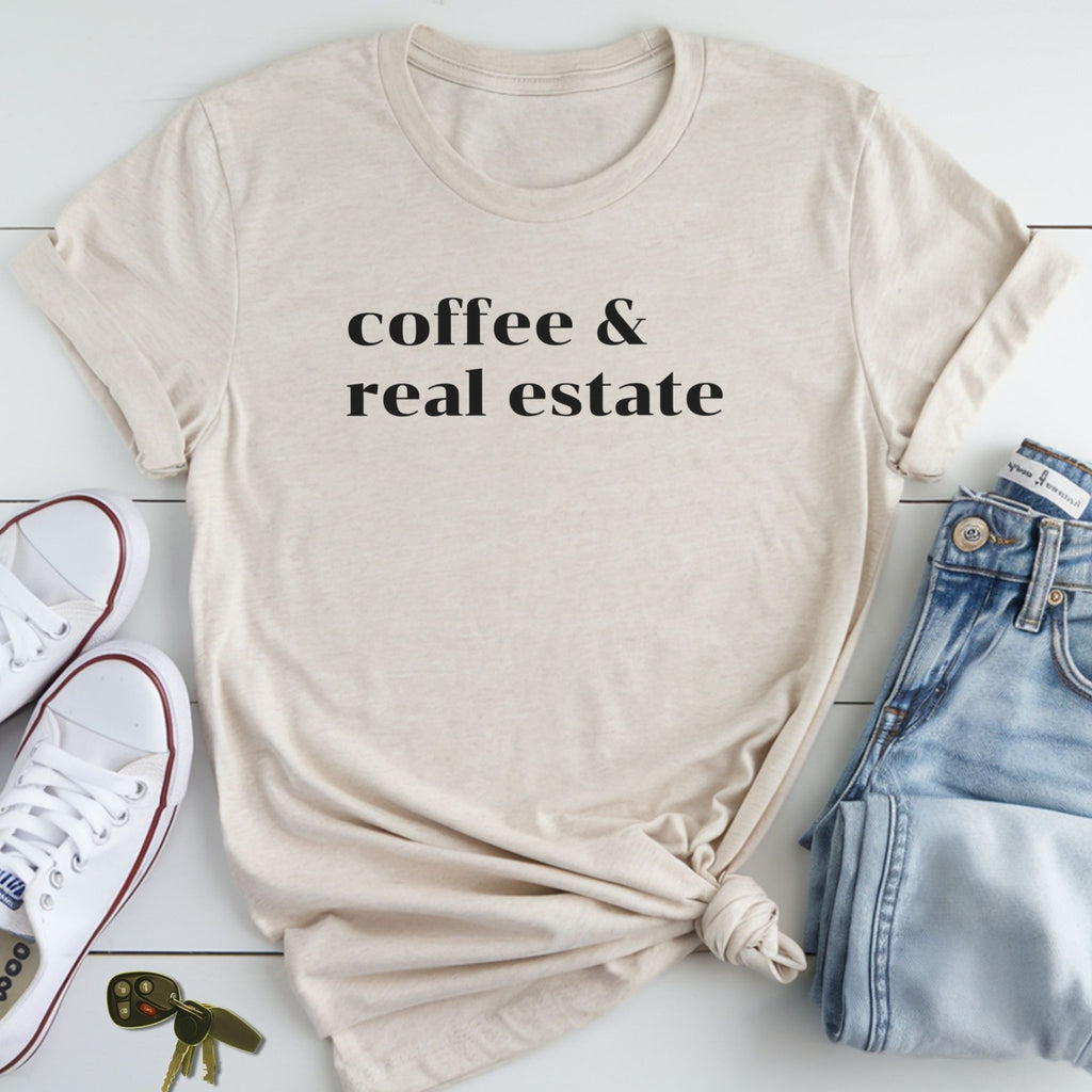 A beige t-shirt with the text "coffee & real estate" printed on it, along with a pair of jeans and white sneakers, all laid out on a white surface.