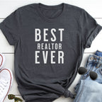 A gray t-shirt with the text "BEST REALTOR EVER" printed on it, along with a pair of jeans and sunglasses.